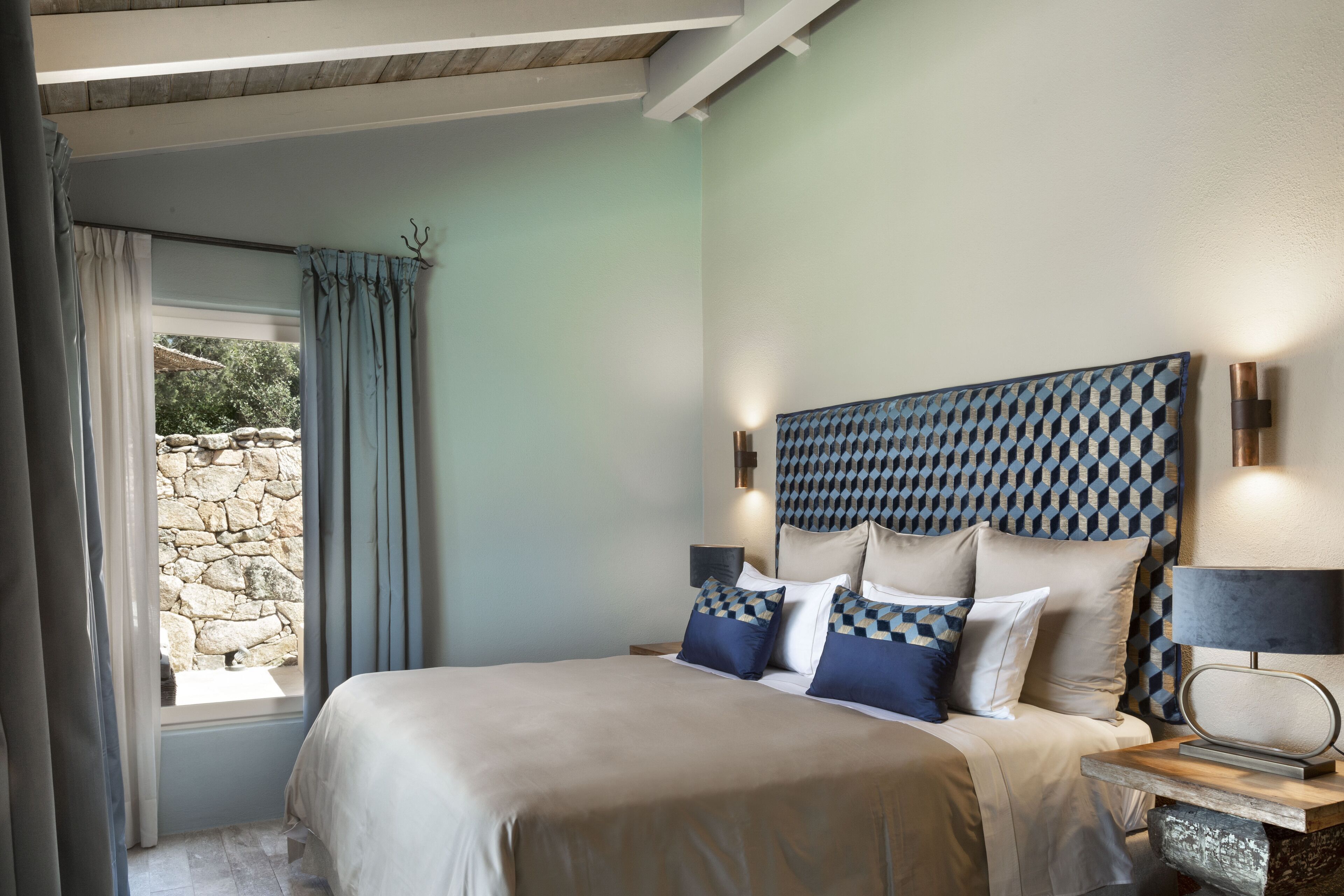 Una camera da letto con un letto, tende, un muro in pietra e una testiera decorata.