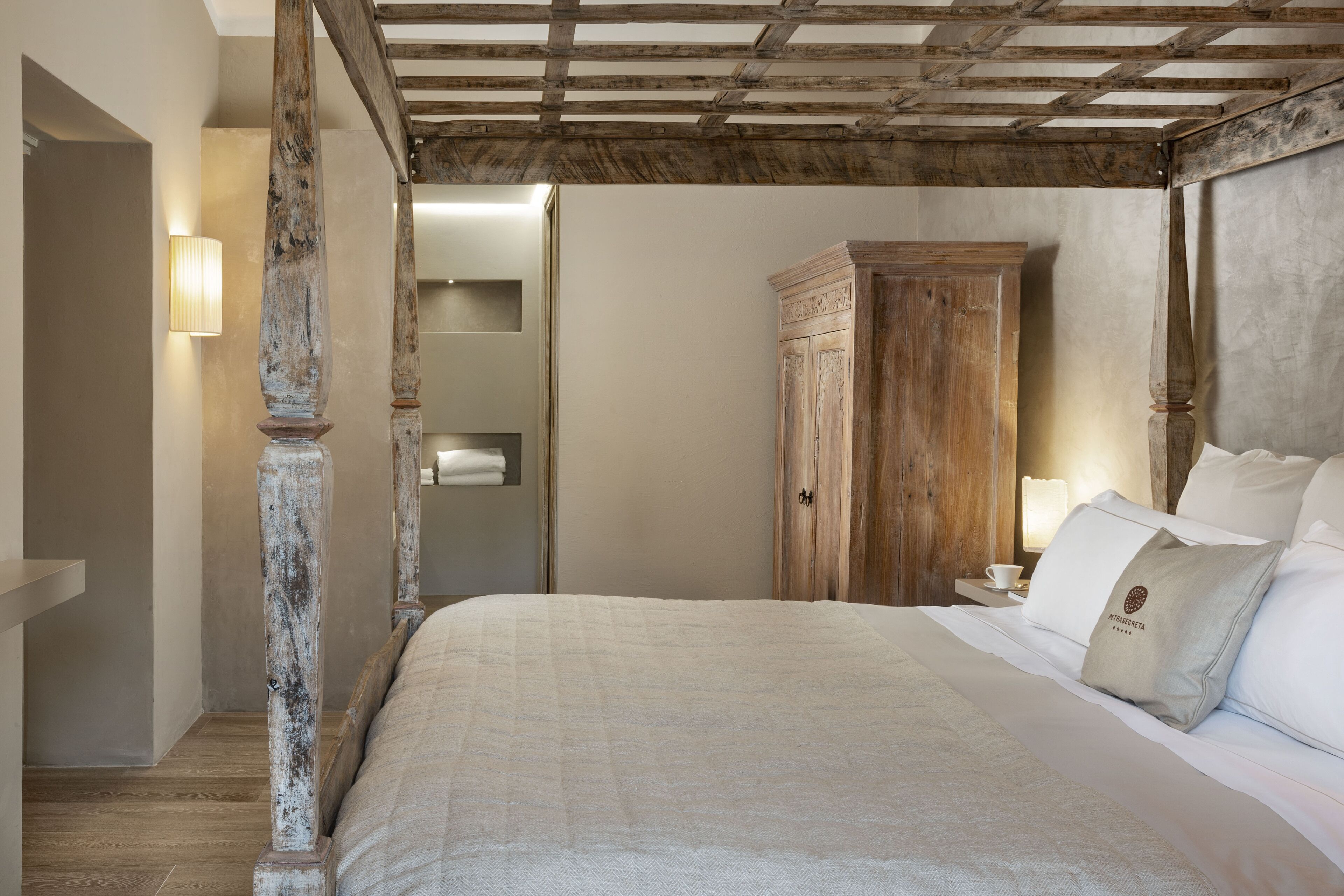 A bedroom with a large bed, wooden wardrobe, and a nightstand with a lamp.