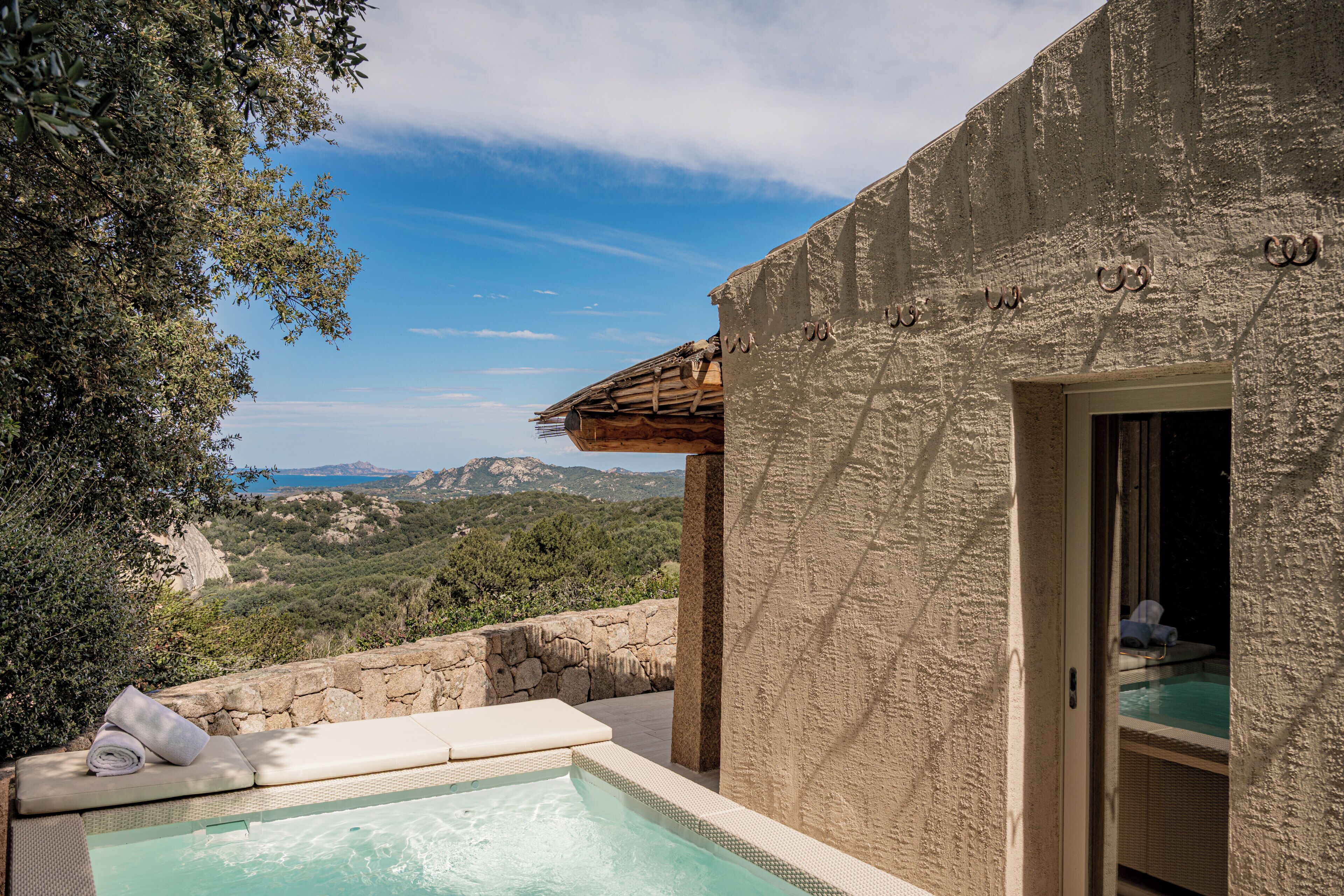 A pool area with a view of mountains, a stone wall, and a building with a textured facade.