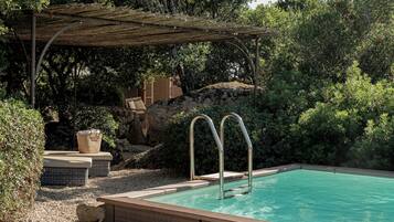 A pool with two metal ladders, surrounded by greenery and a pergola.