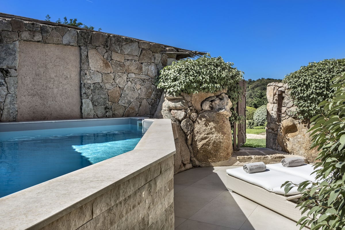A stone-walled swimming pool with a built-in seating area and a stone wall.