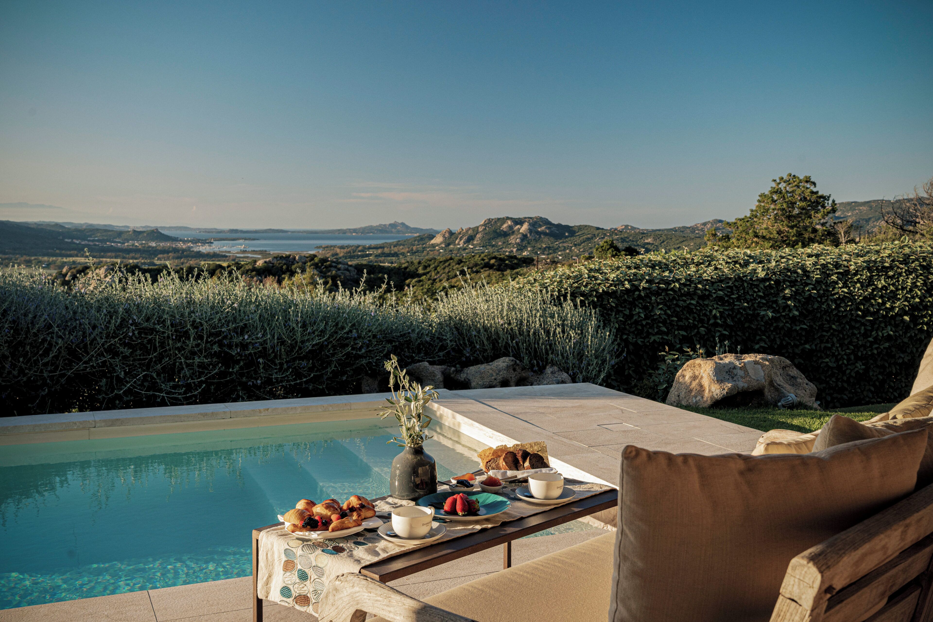 Un área de comedor junto a la piscina con una mesa dispuesta para dos, con vistas a un paisaje pintoresco.