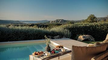 Un área de comedor junto a la piscina con una mesa dispuesta para dos, con vistas a un paisaje pintoresco.