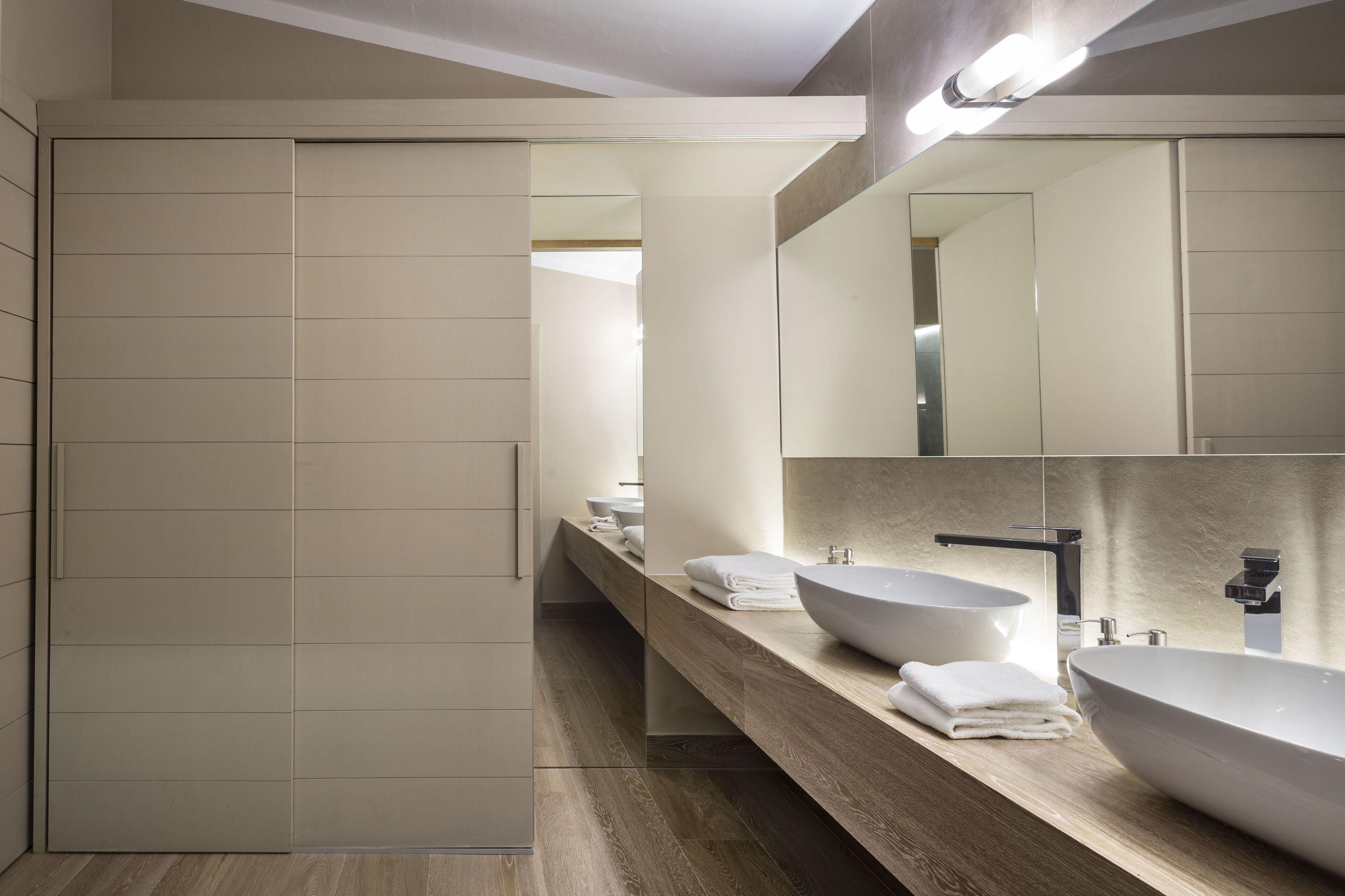A modern bathroom with two large sinks, a mirror, and a wooden vanity.