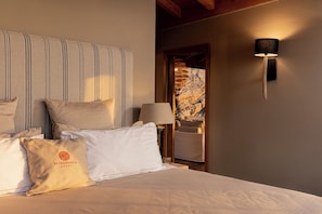 Hotellihuone, jossa on sänky, tyynyt, seinään kiinnitetty valaisin ja näkymä kiviseinälle.