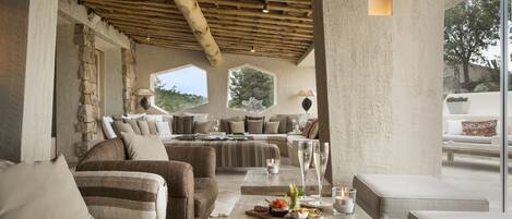 A cozy living area with a stone wall, wooden ceiling, and a large window offering a view of the outdoors.