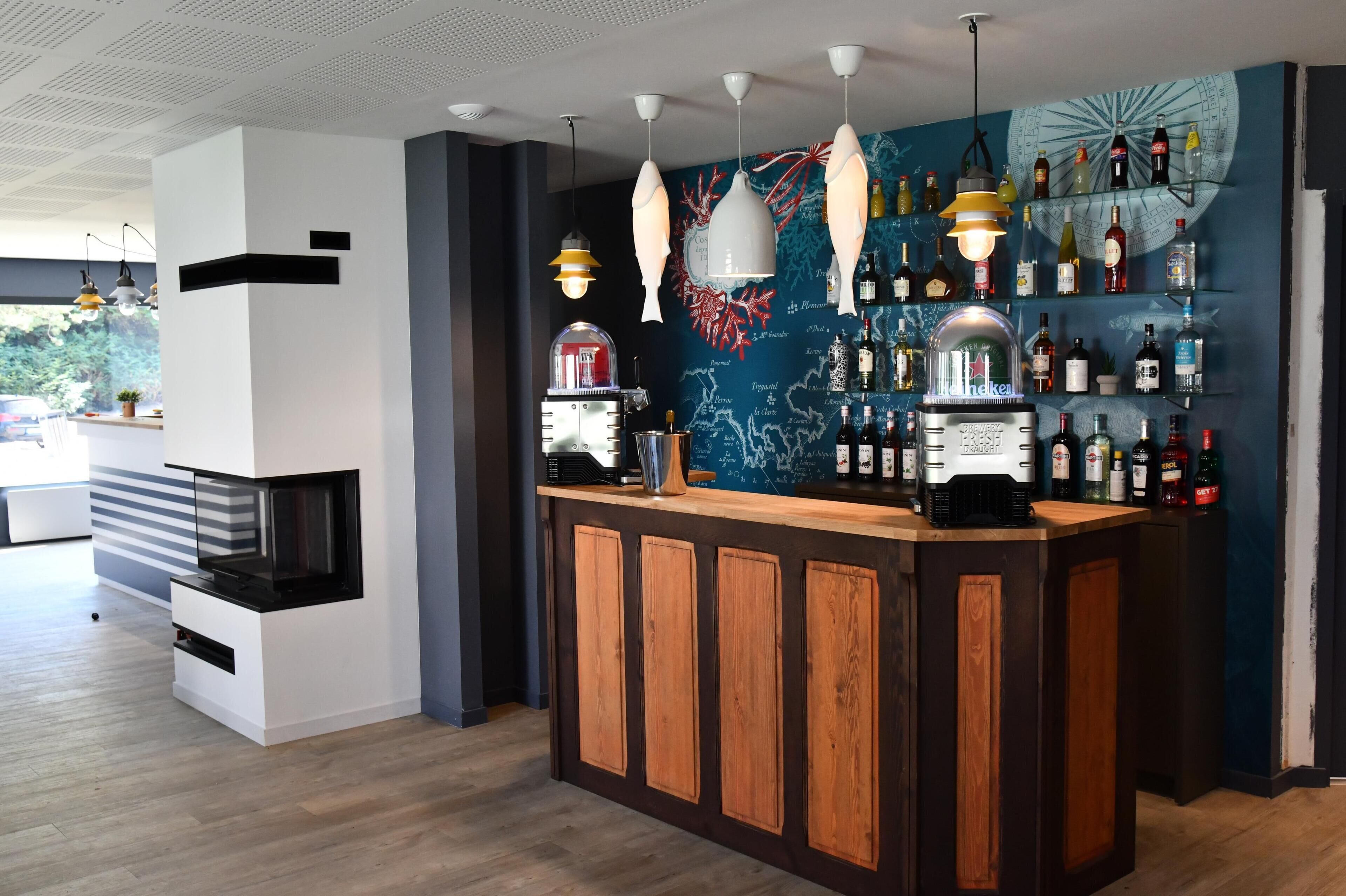 Zona de bar con mostrador de madera, lámparas colgantes y pared con mapa y exhibición de botellas.