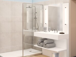 Un baño moderno con ducha de vidrio, tocador blanco con artículos de aseo y espejo sobre el lavamanos.