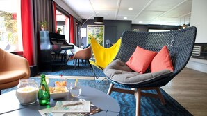 A modern lounge area with a round table, a yellow chair, and a grey chair with orange cushions. - Kyriad Lannion (Lannion)