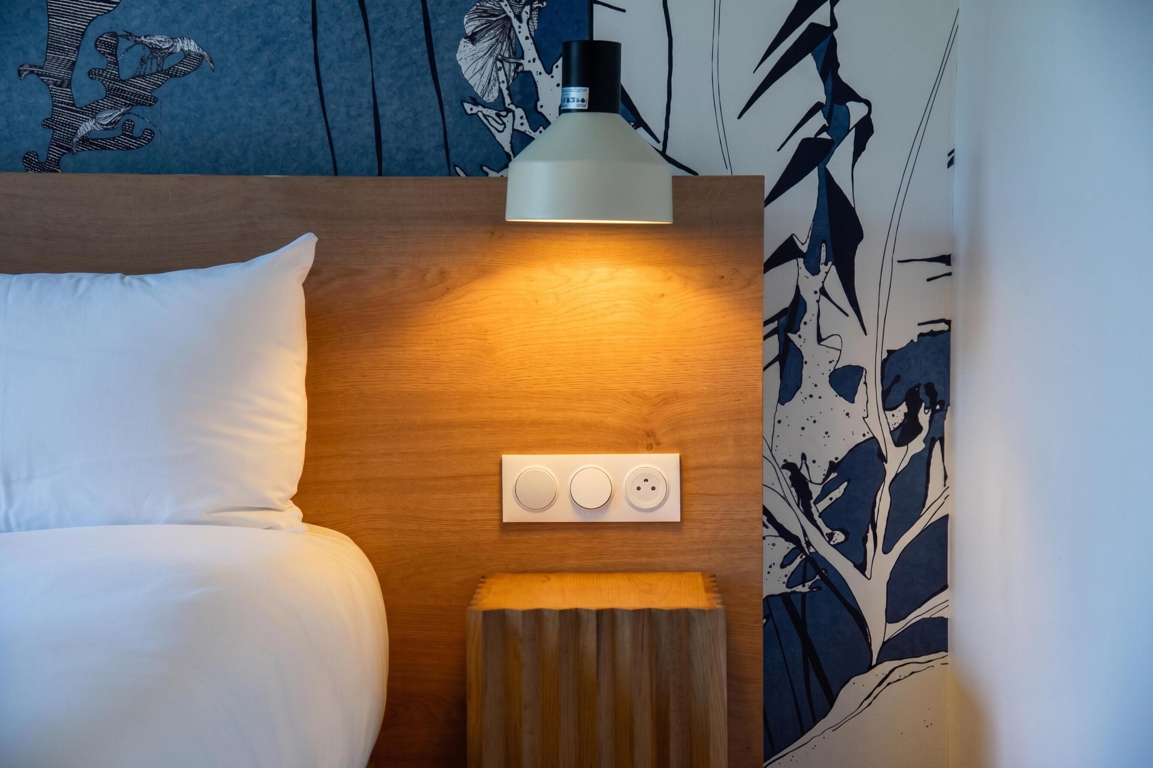 A hotel room with a bed, a bedside table, a lamp, and a power outlet.