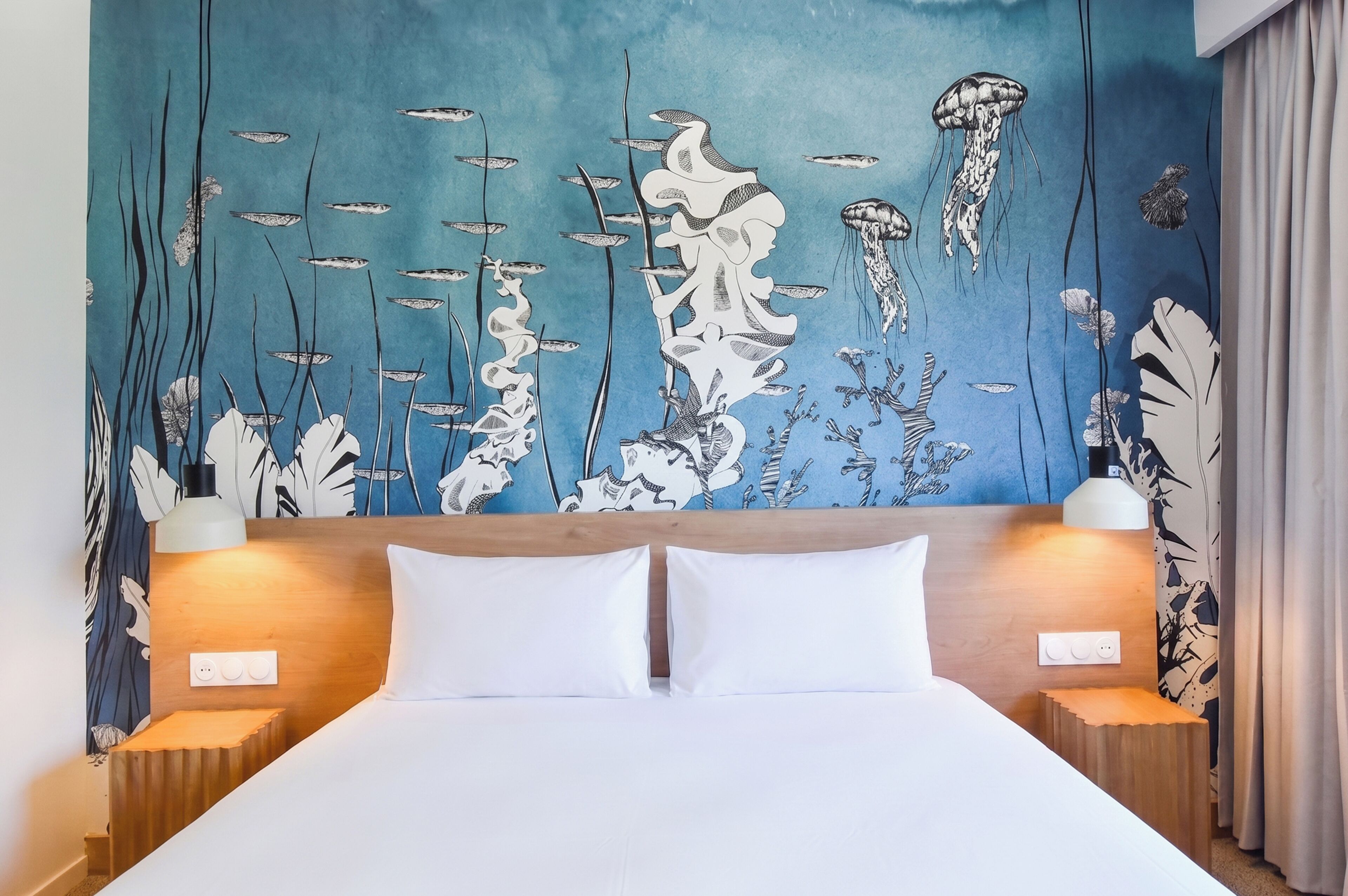 A hotel room with a bed, two bedside lamps, and a wall mural of marine life.