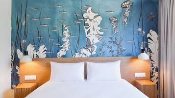 A hotel room with a bed, two bedside lamps, and a wall mural of marine life.
