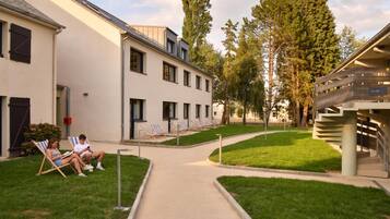 A building with a modern design, featuring a central pathway, outdoor seating area with chairs, and a staircase.