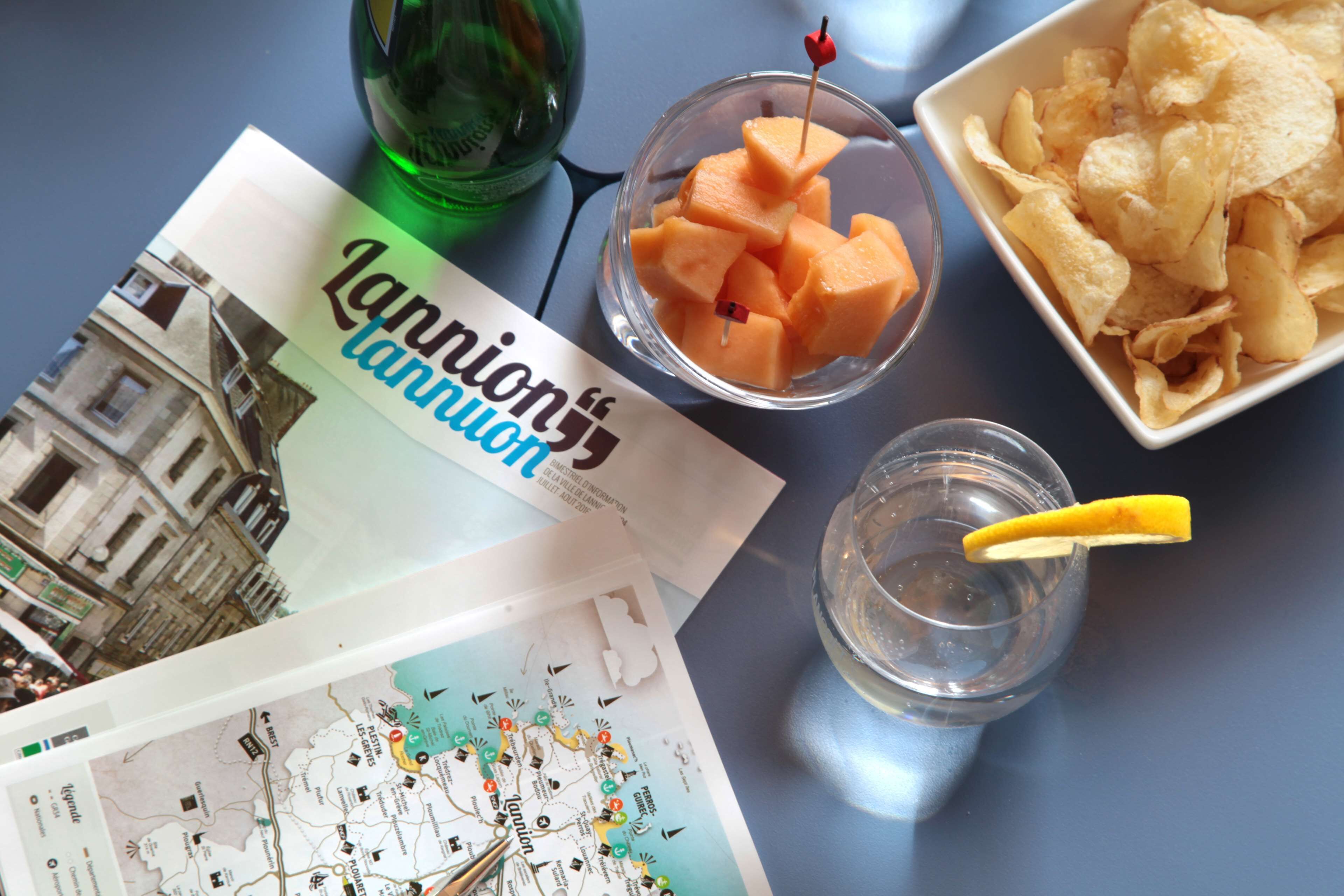A travel map, a bowl of melon cubes, a bowl of chips, and a glass with a lemon slice.