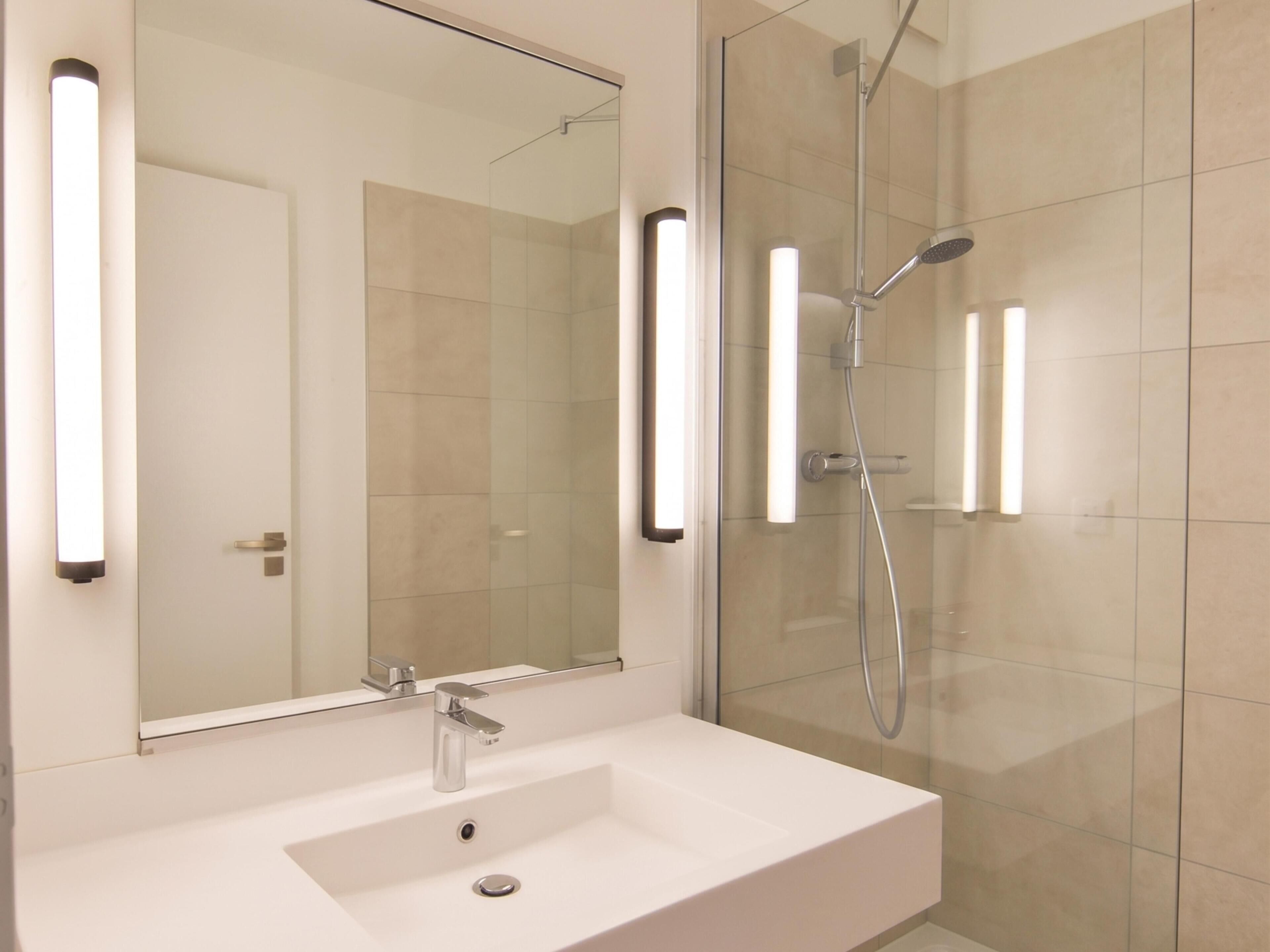 A modern bathroom with a white sink, a mirror, and a glass-enclosed shower area.
