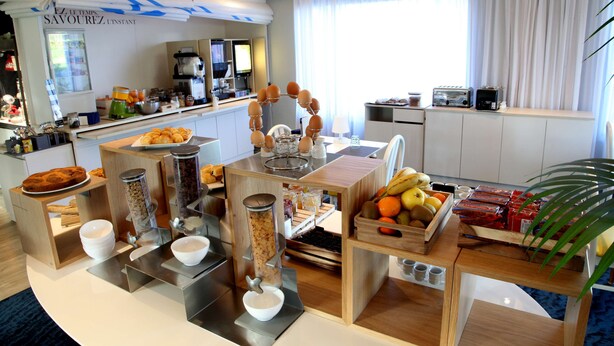 A modern kitchen with a coffee station, breakfast bar, and various food items. - Kyriad Lannion (Lannion)