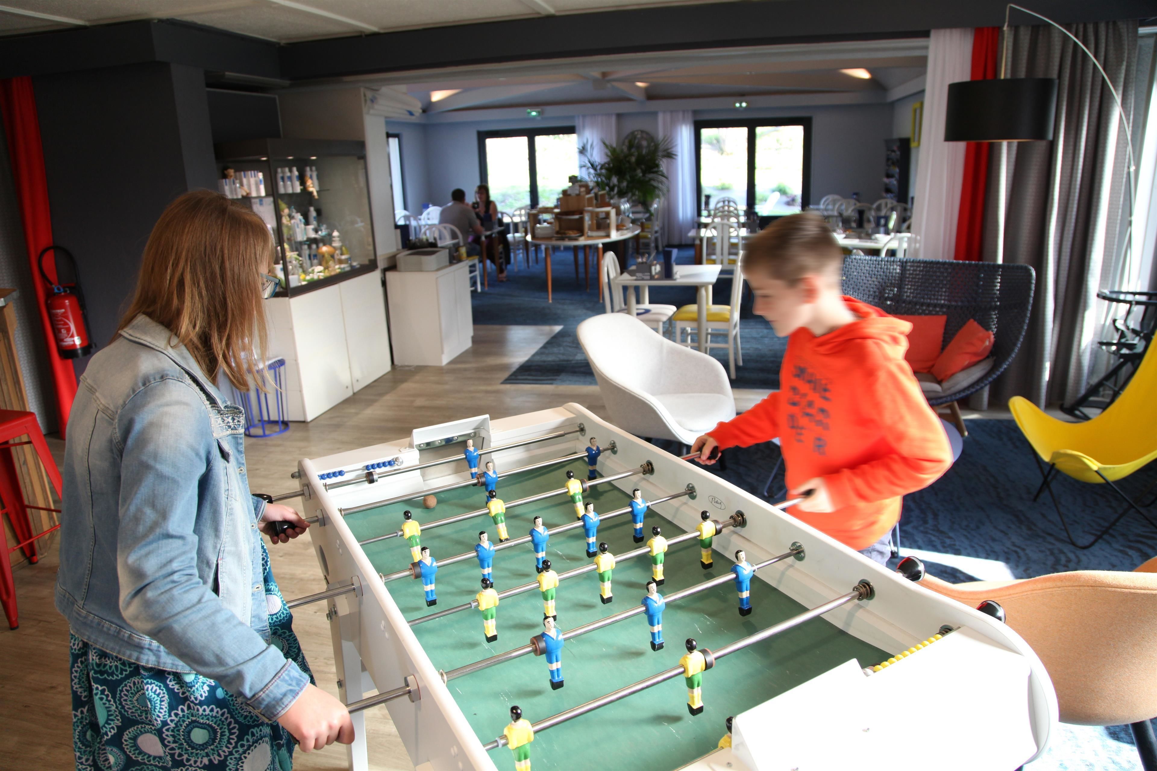 A foosball table in a room with a bar area, seating, and large windows.