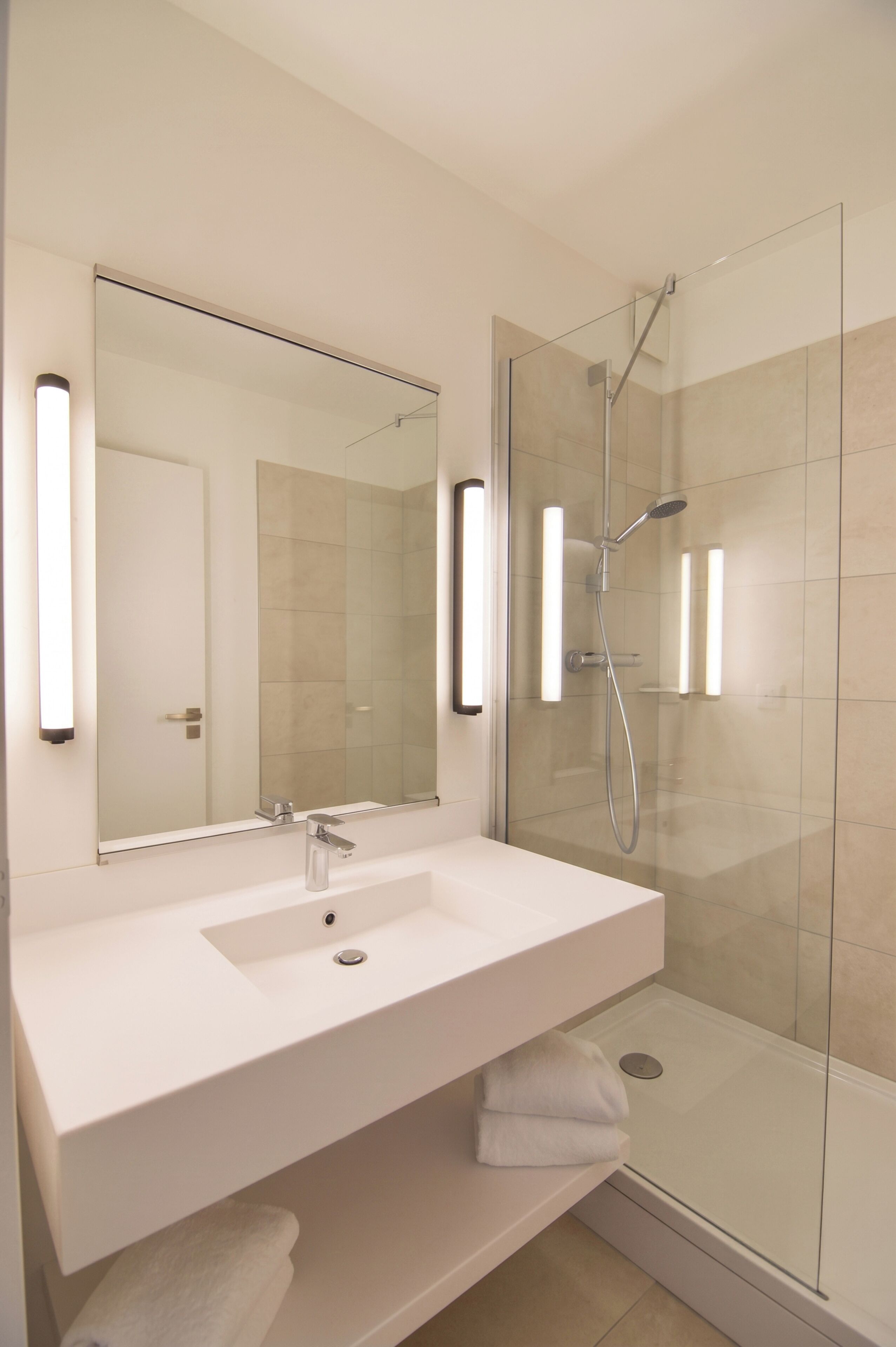 Un baño moderno con un lavamanos blanco, un espejo grande y una ducha con paredes de vidrio.