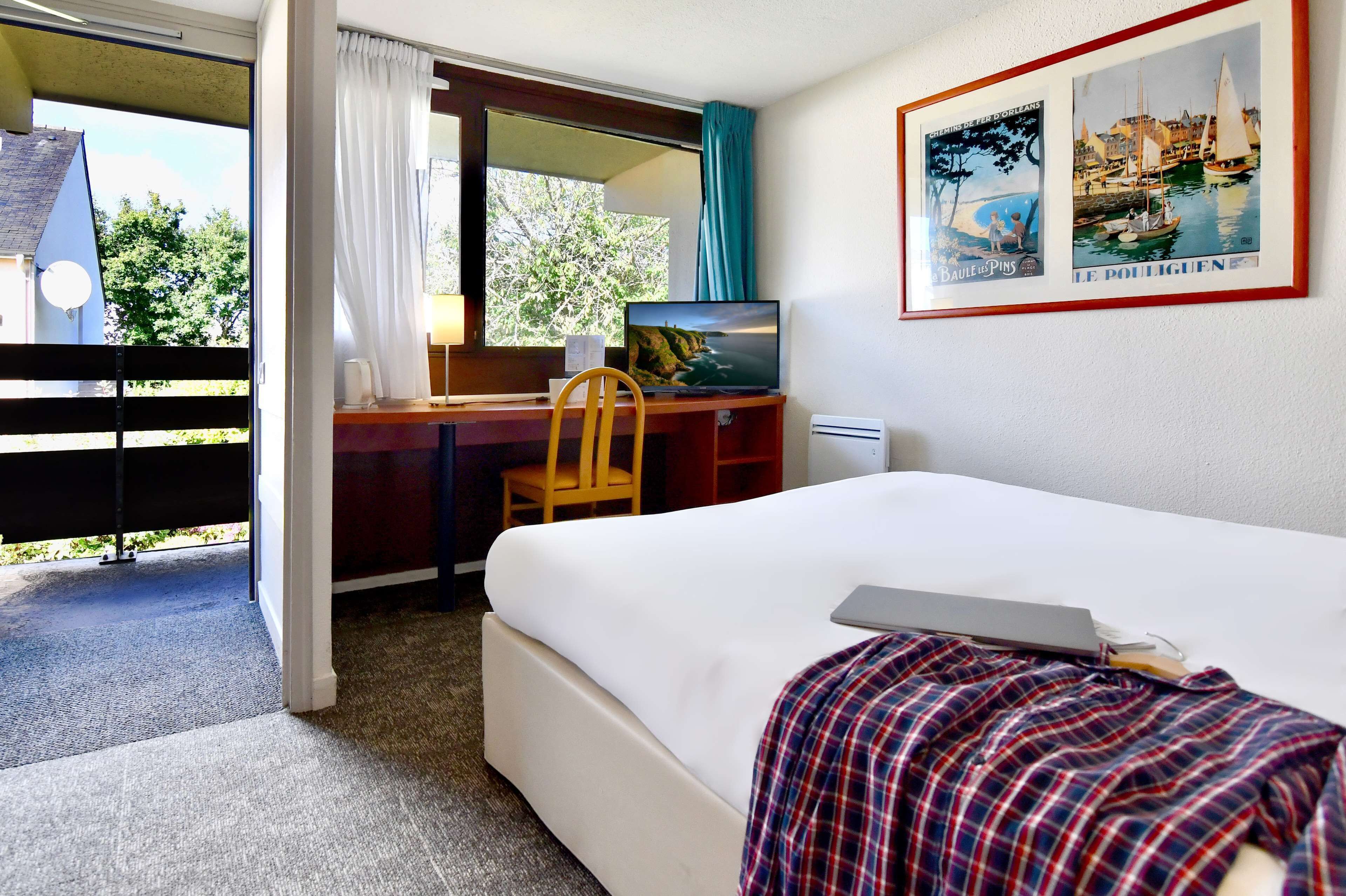 A hotel room with a bed, a desk with a chair, a television, and a window with curtains.