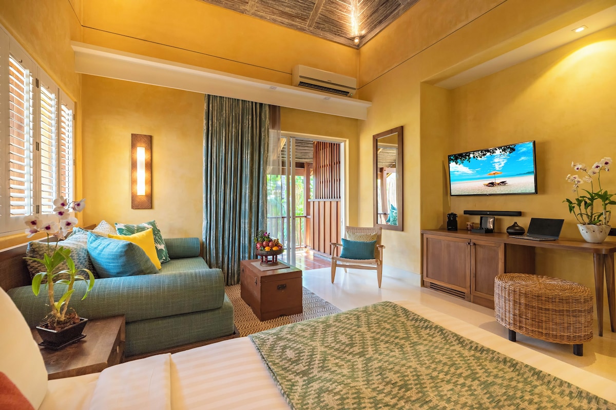 A hotel room with a bed, a sofa, a TV, a desk, and a balcony with curtains.