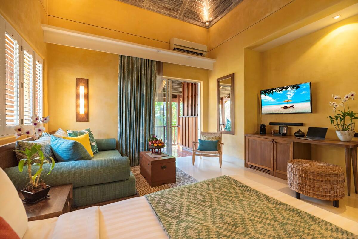 A hotel room with a bed, a sofa, a television, a desk, and a window with blinds.