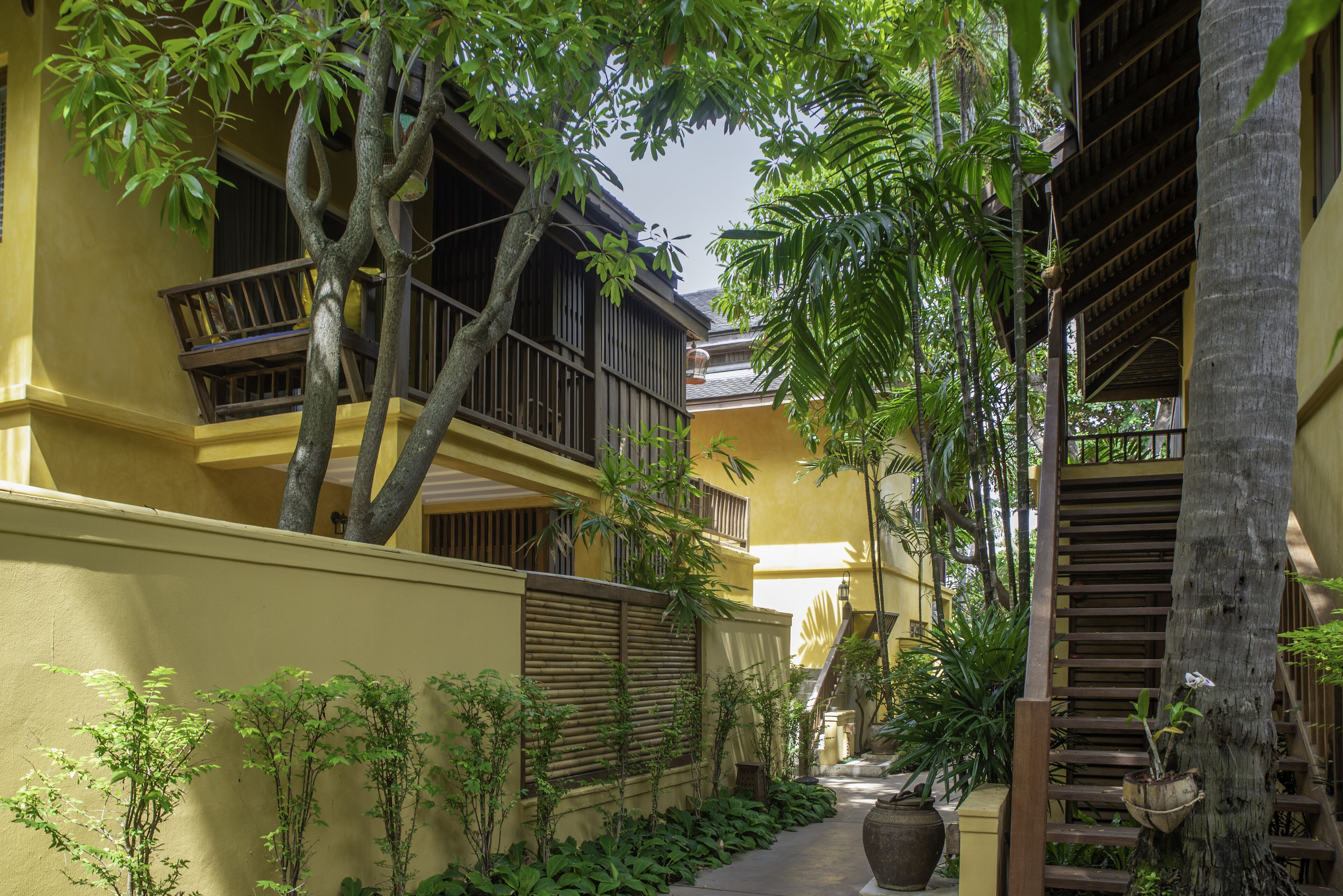 A narrow courtyard with a yellow building, wooden railings, and potted plants.