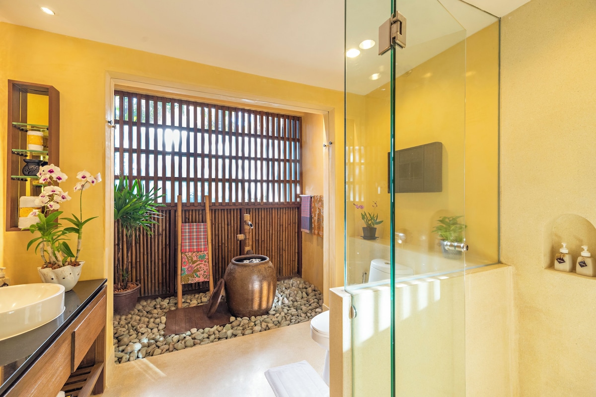 A bathroom with a large sink, a mirror, a glass shower enclosure, and a wooden partition with a bamboo fence.
