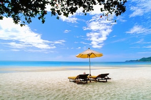 A beach with two sun loungers and a yellow umbrella under a tree.
