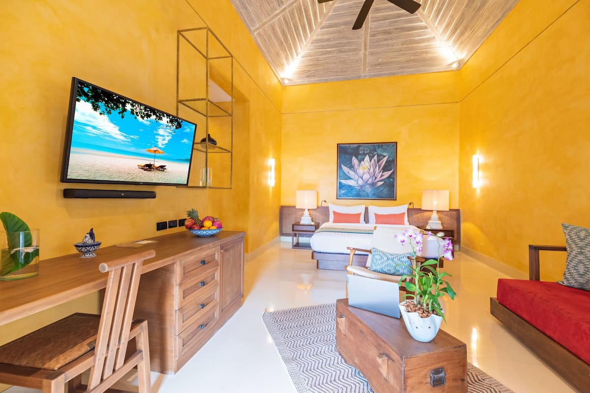 A bright yellow room with a bed, a desk, and a TV.