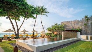 A pool area with lounge chairs and umbrellas, surrounded by a wooden fence and palm trees. - Buri Rasa Village Samui Adults Only (Koh Samui)