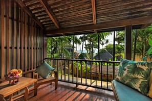 A wooden balcony with a view of palm trees and a beach.