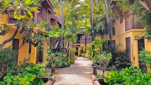A wooden pathway flanked by lush greenery and traditional wooden buildings with balconies. - Buri Rasa Village Samui Adults Only (Koh Samui)