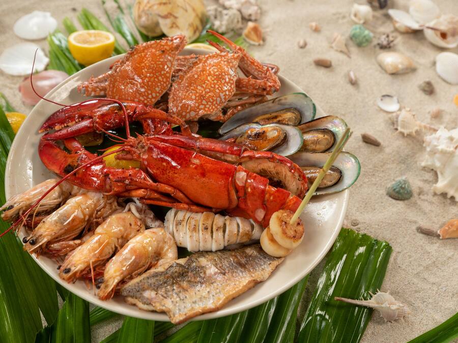 A seafood platter with various shellfish and a fish, garnished with lemon and surrounded by seashells on a plate.