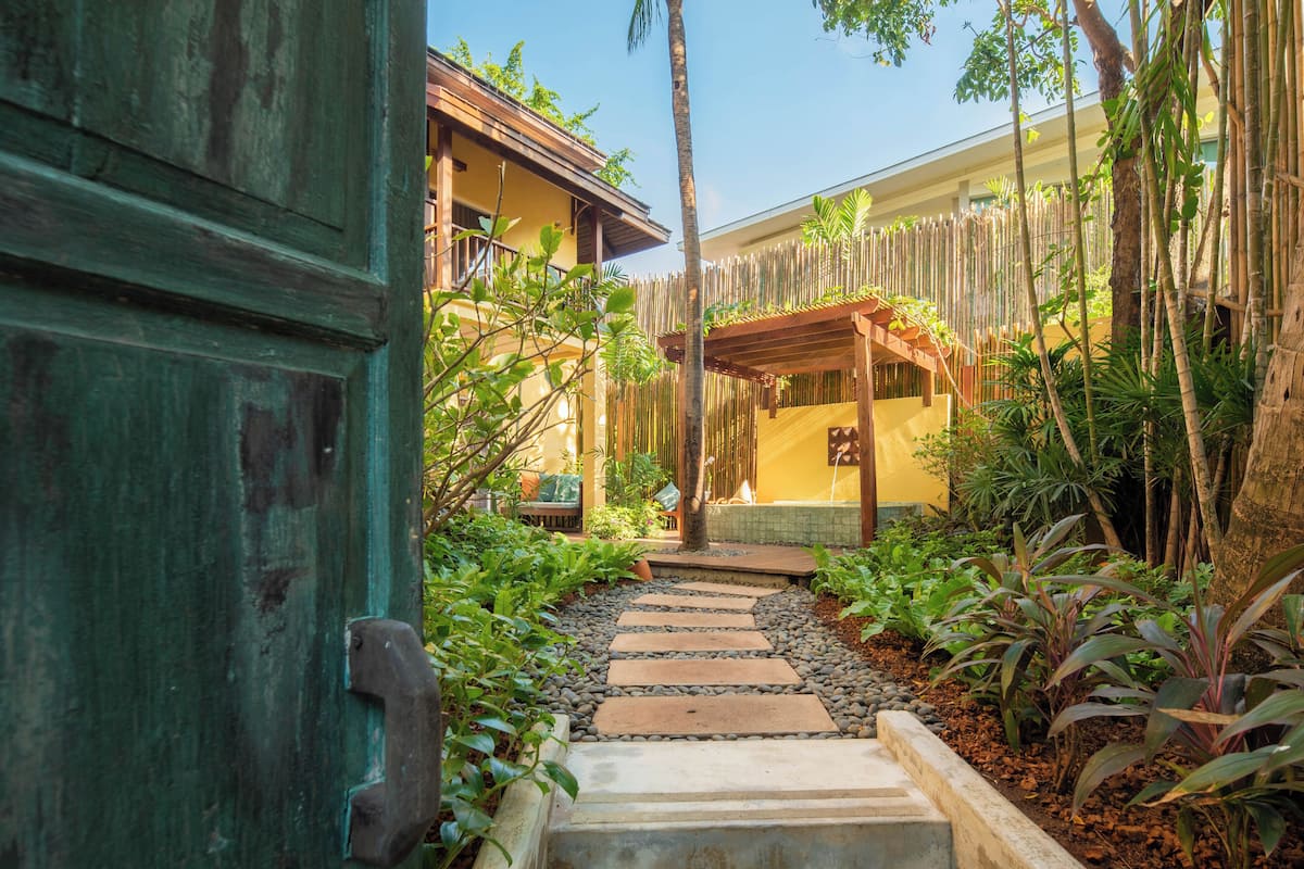 A pathway leading to a building with a bamboo fence and tropical plants.