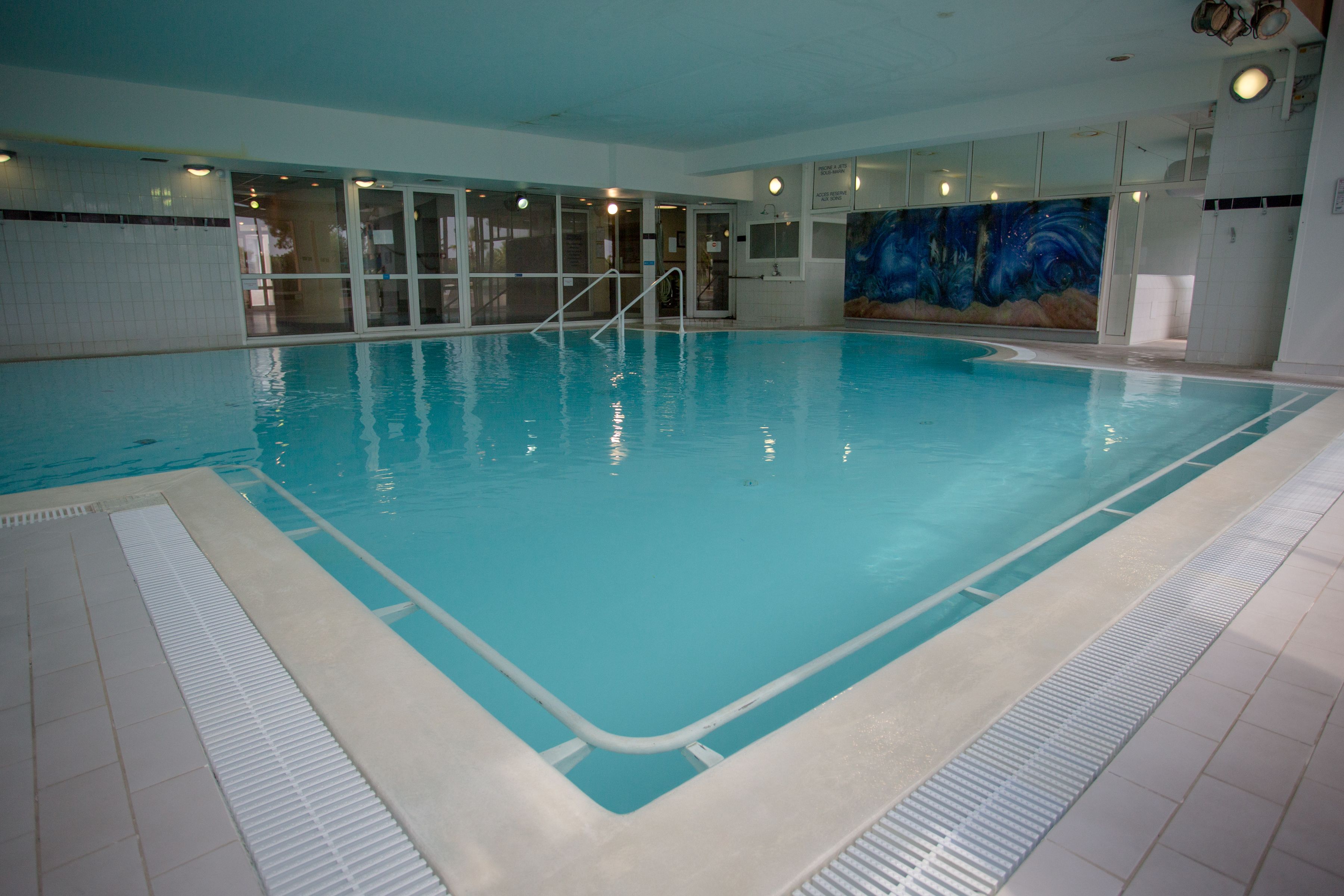 Ein Hallenbad mit klarem Wasser, gefliesten Wänden und einem Wandgemälde an einer Seite.