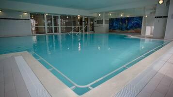 Ein Hallenbad mit klarem Wasser, gefliesten Wänden und einem Wandgemälde an einer Seite.