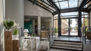 Eine moderne Hotelhalle mit Glasdach, Holzboden und einer Treppe, die zu einer Außen-Sitzgelegenheit führt.