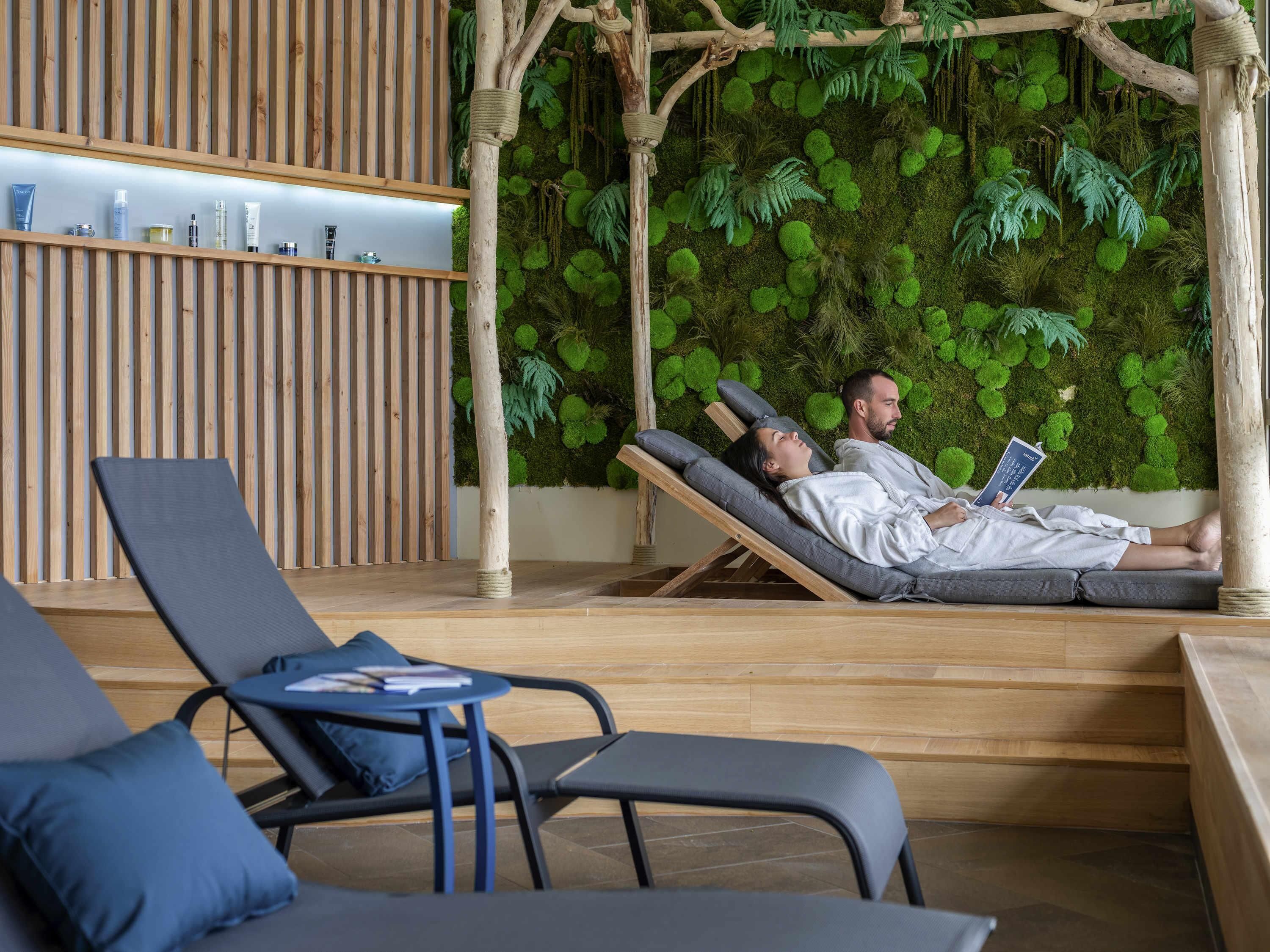Een wellnessruimte met houten lambrisering, een groene moswand en comfortabele fauteuils.