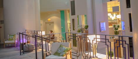 A spacious indoor area with a high ceiling, wooden flooring, and a seating area with chairs and ottomans.