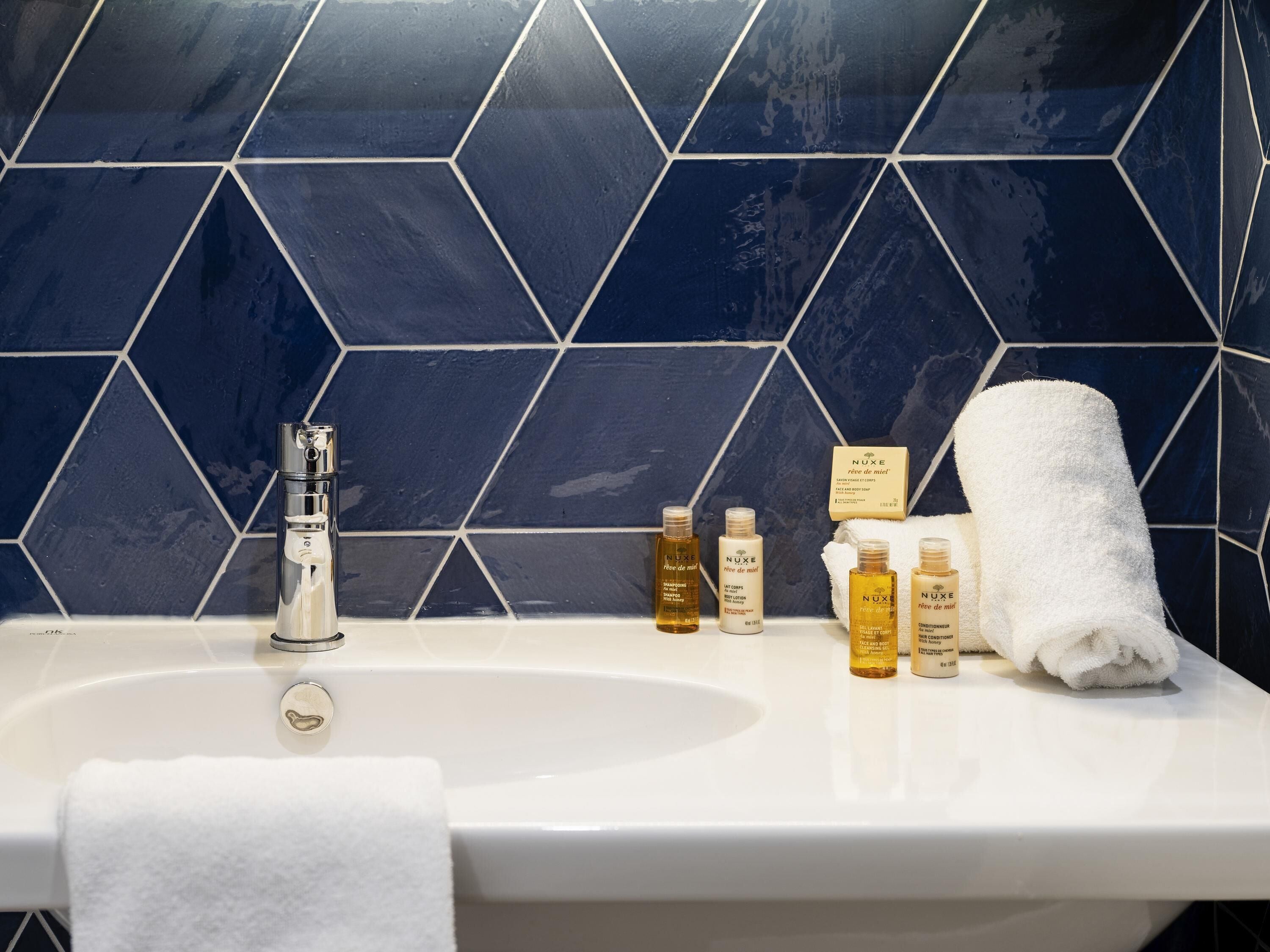 Ein Badezimmer mit einem weißen Waschbecken, einem Spiegel und einer blau gefliesten Wand.