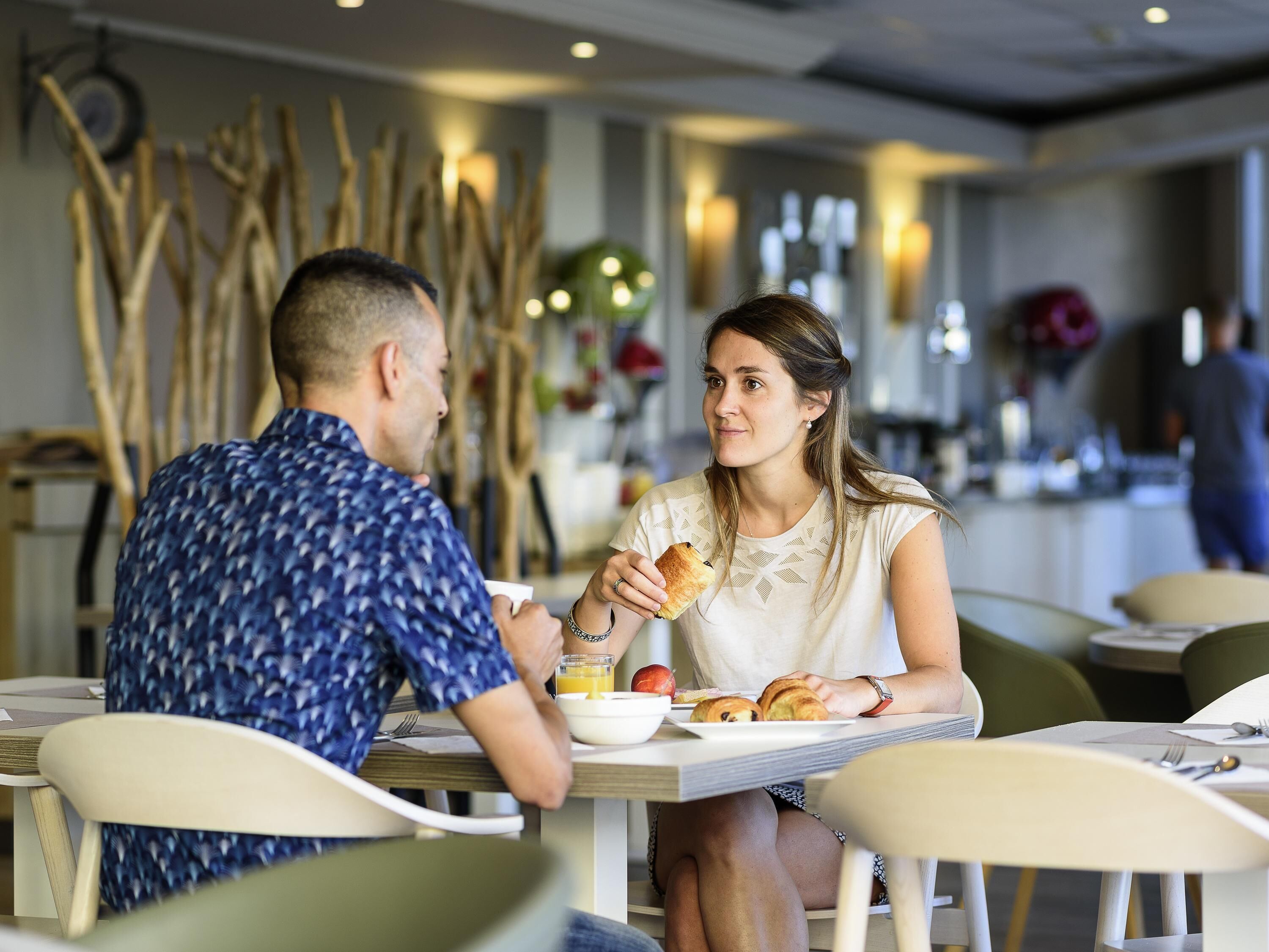 Un couple est assis à une table dans un restaurant au décor moderne, avec des chaises, une table et un mur décoratif agrémenté d’éléments verticaux.