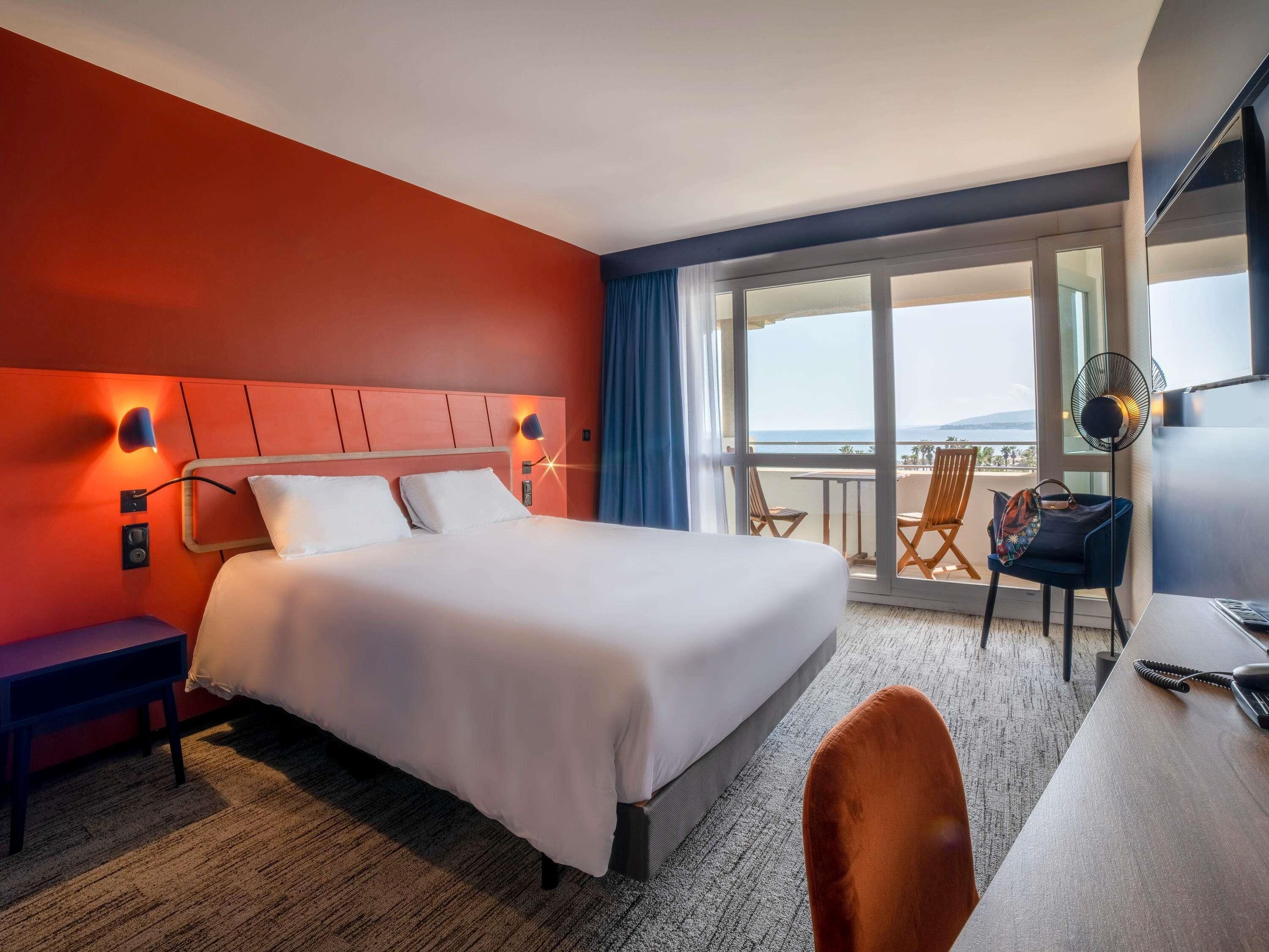 Ein Hotelzimmer mit Bett, Schreibtisch, Stuhl und einem Balkon mit Blick.