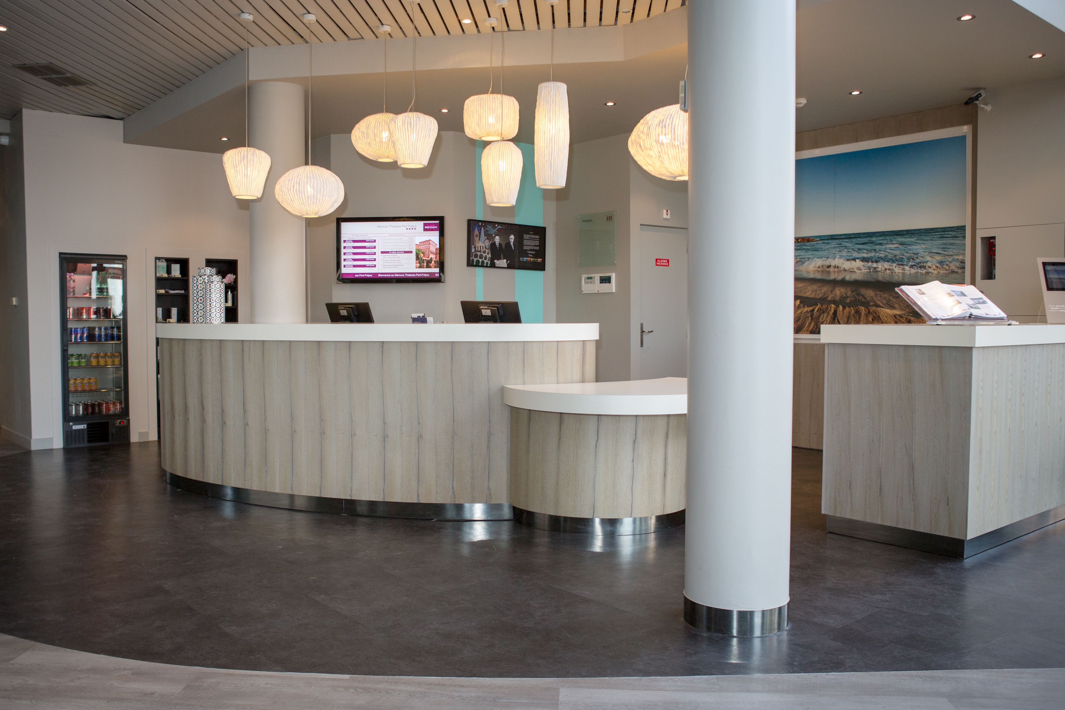 A reception area with a curved counter, pendant lighting, a digital display, and a large wall mural.