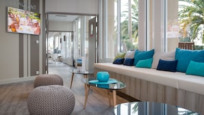 Ein modernes Interieur mit einer Sitzecke, einem Fernseher, der eine Restaurantszene zeigt, und großen Fenstern mit Blick auf Palmen.