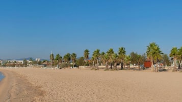 Una playa con arena, palmeras y edificios al fondo.