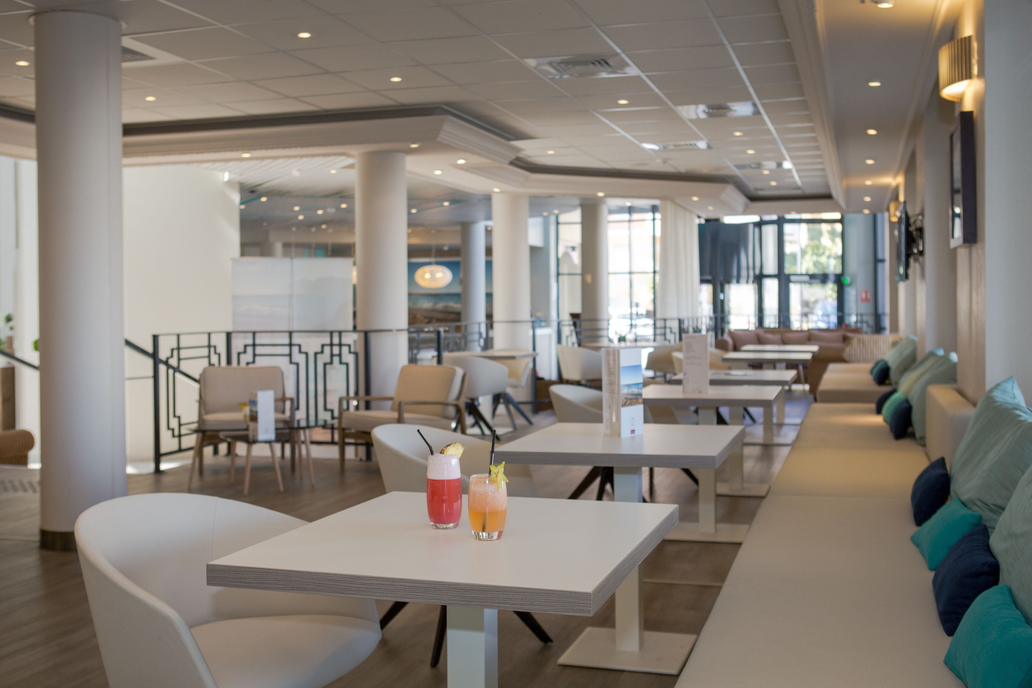 A spacious indoor area with multiple seating arrangements, including tables and chairs, and a long bench with cushions.