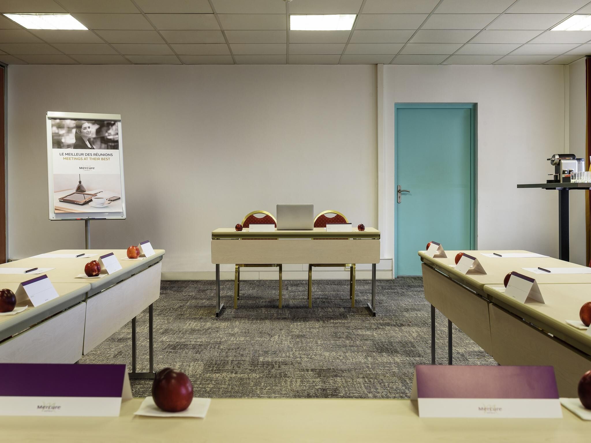 A conference room with a long table, nameplates, and apples. There is a poster on the wall and a door in the background.