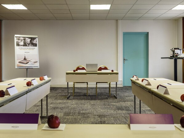 Une salle de conférence avec une longue table, des plaques nominatives et des pommes. Il y a une affiche au mur et une porte à l’arrière-plan.