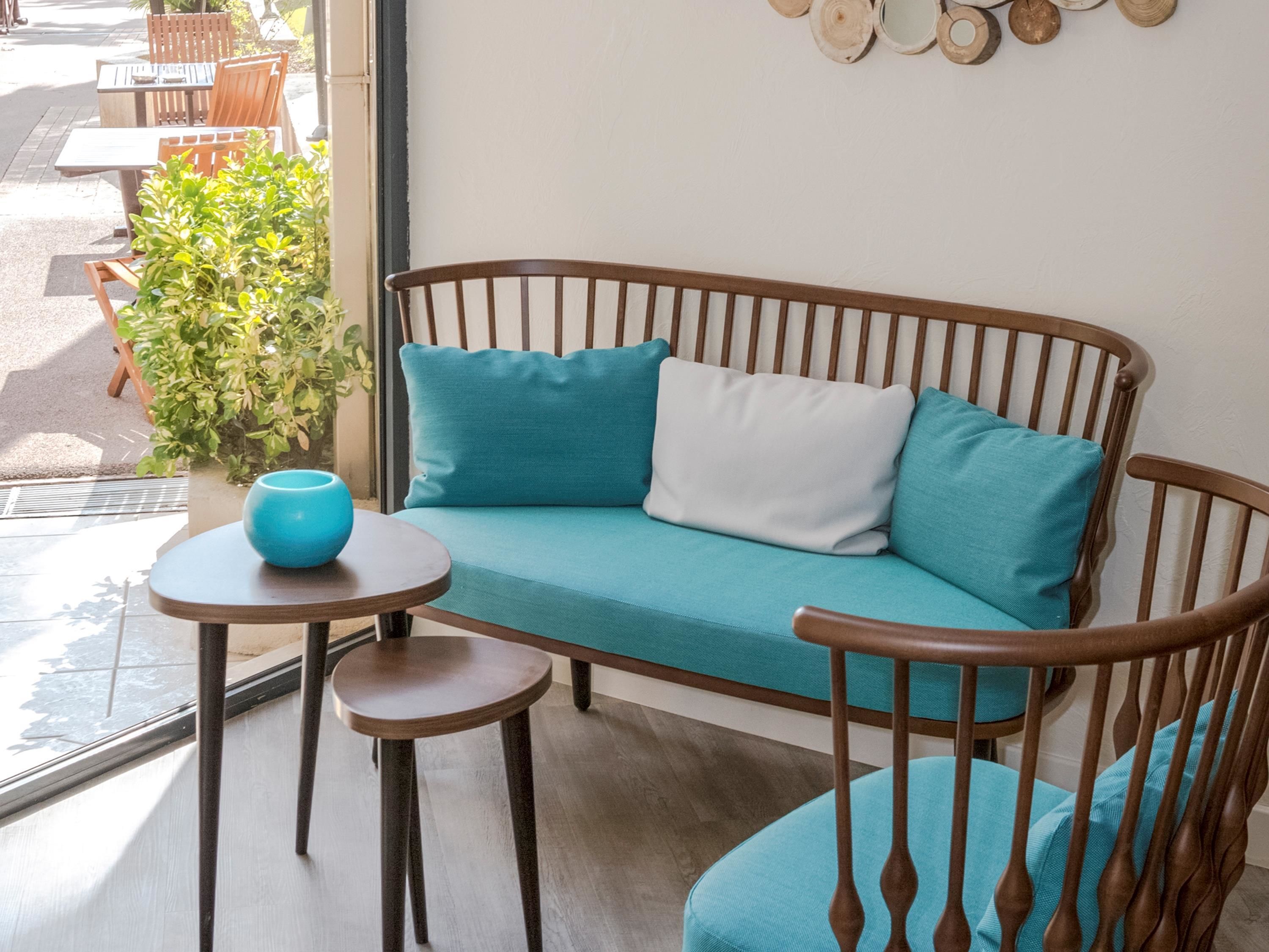 Un banco de madera con cojines color turquesa, una mesita redonda con un cuenco azul y una planta en maceta.