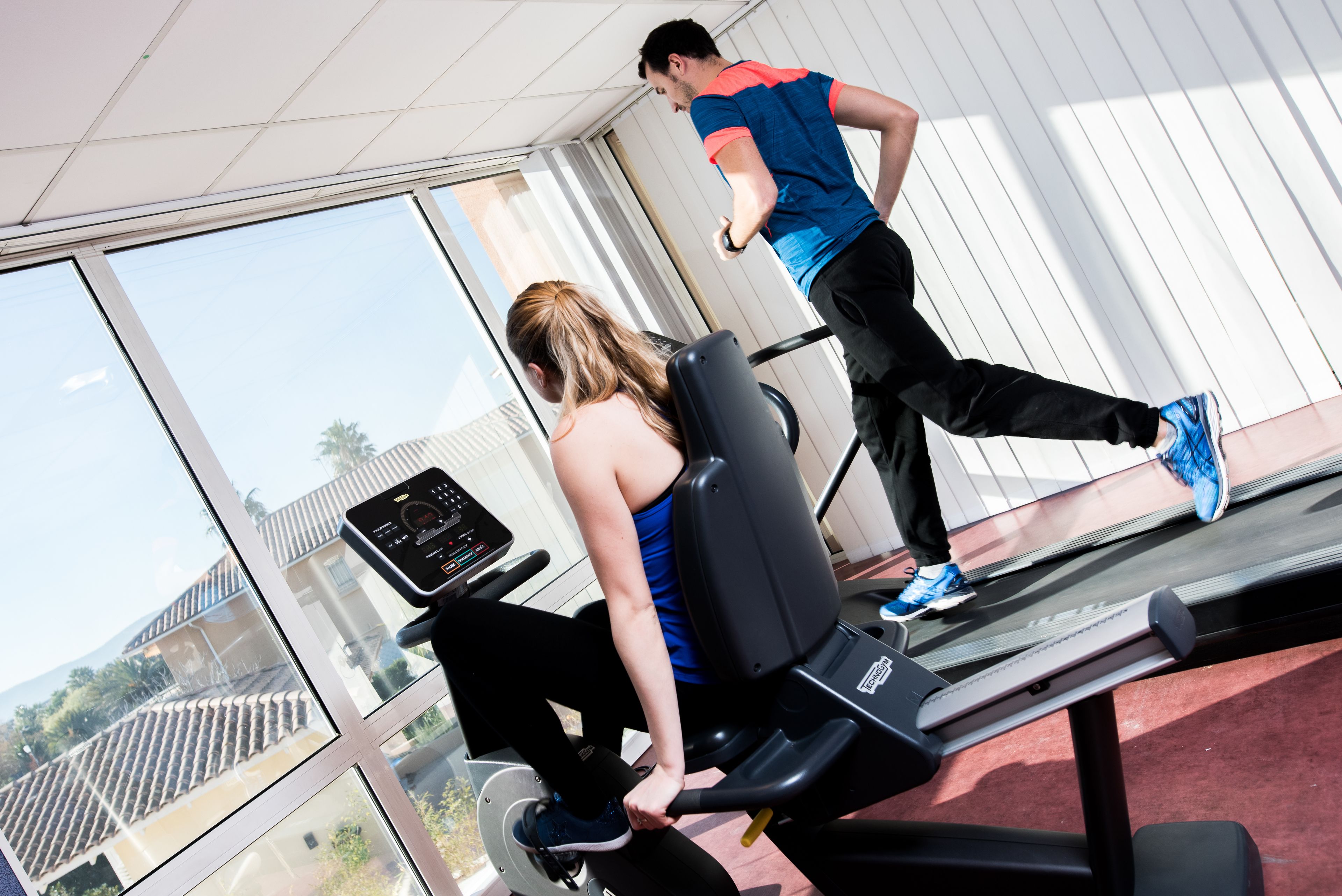 Une salle de sport équipée de tapis de course et d’appareils d’exercice, dotée de grandes fenêtres et offrant une vue sur les bâtiments environnants.